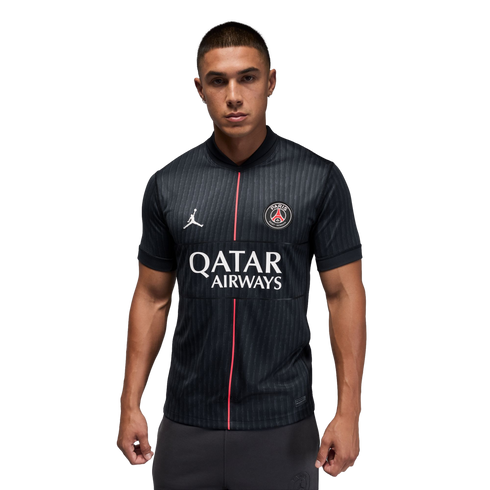 Man modeling a black PSG jersey with a thin vertical pink stripe and Qatar Airways logo against a black background.