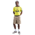 A man models a yellow Tottenham Hotspur football jersey, tan cargo shorts, and grey sneakers against a black background.