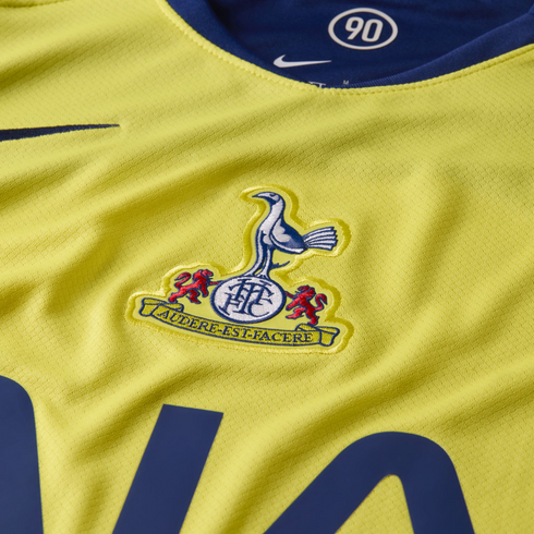 Close-up of a yellow Nike soccer jersey featuring the Tottenham Hotspur crest and motto. The blue collar shows a white "90" graphic.