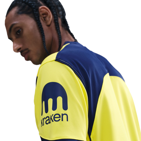Profile of a person with braided hair wearing a yellow and blue jersey featuring the Kraken logo on the sleeve.