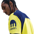 Profile of a person with braided hair wearing a yellow and blue jersey featuring the Kraken logo on the sleeve.