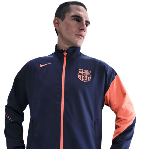 A man in a navy and orange Nike FC Barcelona track jacket against a black background.
