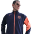 A man in a navy and orange Nike FC Barcelona track jacket against a black background.