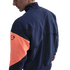 Side view of a person wearing a navy blue Nike jacket with a prominent orange sleeve panel against a black background.