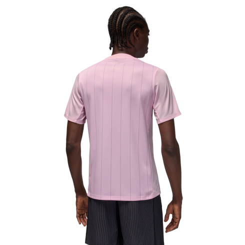 Rear view of a person with braided hair wearing a light pink pinstriped t-shirt and dark pinstriped shorts against a solid black background.