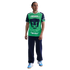 A man wearing a green and navy Pumas soccer jersey, navy sweatpants, and light blue sneakers stands against a black background.
