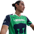 Man with hair in a bun wearing a green and navy Nike Pumas UNAM soccer jersey with a DHL logo, looking to the side.
