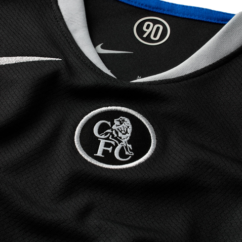 Close-up of a black Nike Chelsea FC jersey featuring a silver embroidered crest and a "90" logo inside the white-trimmed collar.