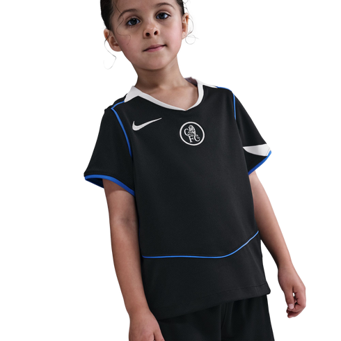 A young child wearing a black Nike Chelsea FC football kit with blue and white trim, standing against a solid black background.