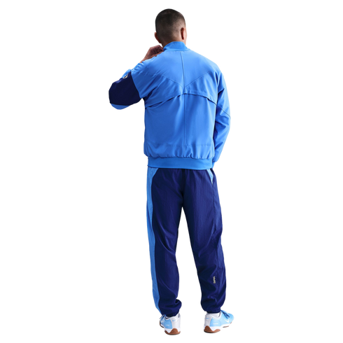 Rear view of a person wearing a two-tone blue Nike tracksuit and matching sneakers against a black background.