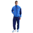 A man wearing a light blue and navy Nike Tottenham Hotspur FC tracksuit and matching sneakers, standing against a solid black background.
