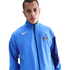 A man wearing a light blue Nike Tottenham Hotspur track jacket against a solid black background.