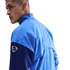 A man looking over his shoulder in a light blue and navy Nike jacket with a gold logo on the arm, set against a black background.