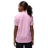 Rear view of a person with a curly ponytail wearing a light pink, pinstriped t-shirt and black shorts against a black background.