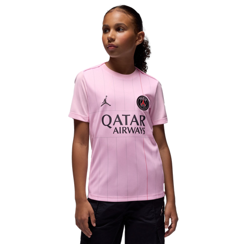 Young girl models a pink PSG jersey with Qatar Airways and Jordan logos against a solid black background.
