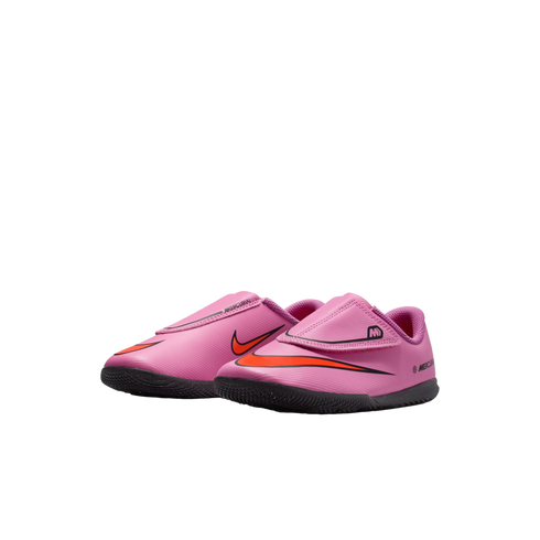 A pair of pink toddler Nike Mercurial indoor soccer shoes with orange swooshes and black soles, isolated on a black background.
