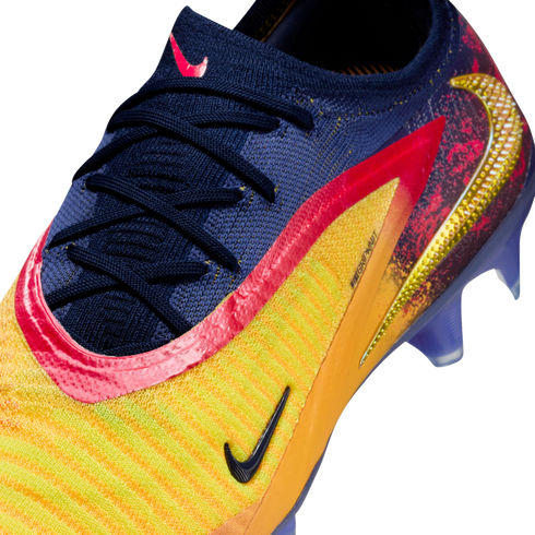 Close-up of a Nike soccer cleat featuring a navy blue knit upper, yellow and orange stripes, pink accents, and a textured gold Swoosh logo.