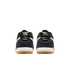 Rear view of two black Nike sneakers with gold script logos on the heels, white midsoles, and tan gum outsoles against a solid black background.