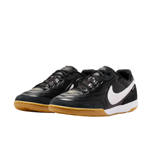 A pair of black Nike indoor soccer shoes with white swooshes and gum rubber outsoles, shown against a solid black background.