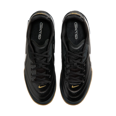 Top-down view of black Nike Tiempo Gato sneakers featuring gold accents and gum rubber outsoles on a solid black background.