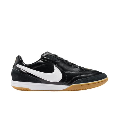 Profile of a black Nike Tiempo indoor soccer shoe with a white swoosh, white midsole, and gum rubber outsole, displayed against a black background.
