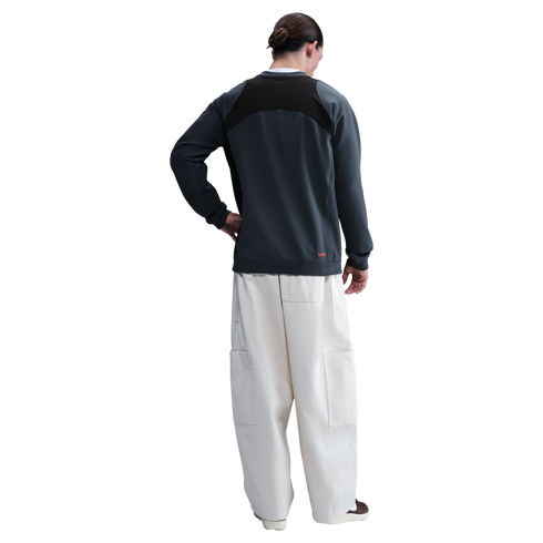 Rear view of a person wearing a dark grey panelled sweatshirt and cream wide-leg cargo pants against a black background.