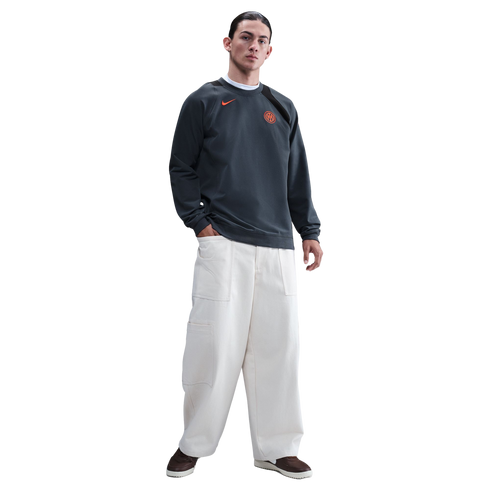 A man wearing a dark grey Inter Milan Nike sweatshirt and wide-leg off-white trousers against a black background.