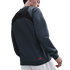 A man seen from behind wearing a grey and black color-blocked sweatshirt with a red logo on the hem and white pants.