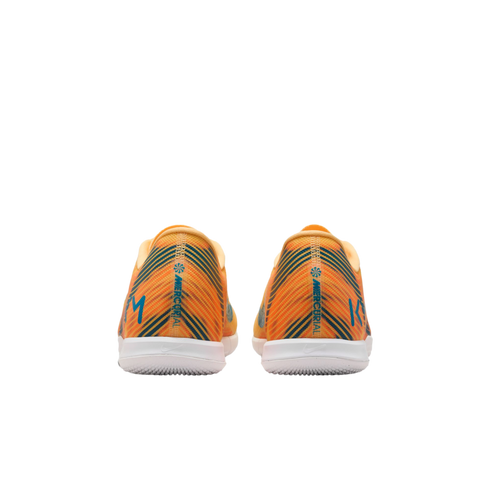 Back view of orange Nike Mercurial soccer shoes featuring blue diagonal stripes, white soles, and "KM" branding on the heels.