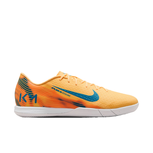 A Nike Mercurial indoor soccer shoe in light orange with blue accents and Kylian Mbappé "KM" branding on the heel, set against a black background.