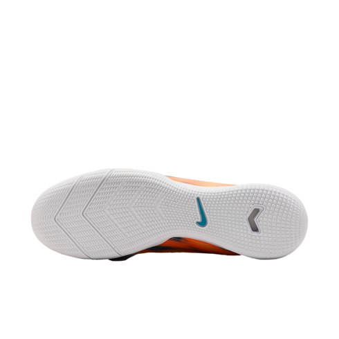 Bottom view of a white Nike soccer shoe outsole with textured tread, featuring a blue swoosh logo and glimpses of an orange upper against a black background.