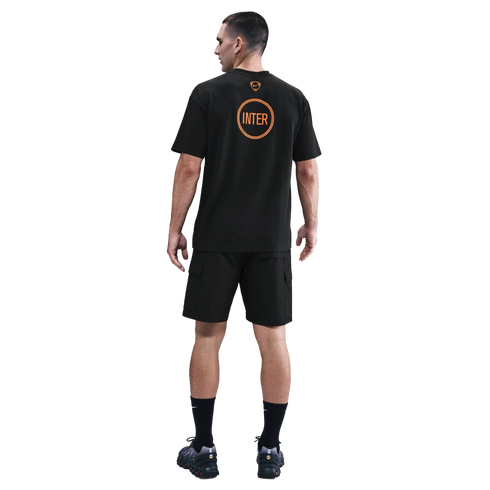 Rear view of a man wearing a black Nike Inter Milan T-shirt with orange graphics, black cargo shorts, and black sneakers on a plain black background.