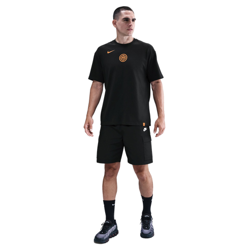Man standing in a black Nike Inter Milan t-shirt with orange logos, black cargo shorts, and black sneakers against a solid black background.