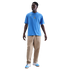 Full-length portrait of a man wearing a light blue Nike Tottenham Hotspur t-shirt, tan trousers, and blue and white sneakers, standing against a solid black background.