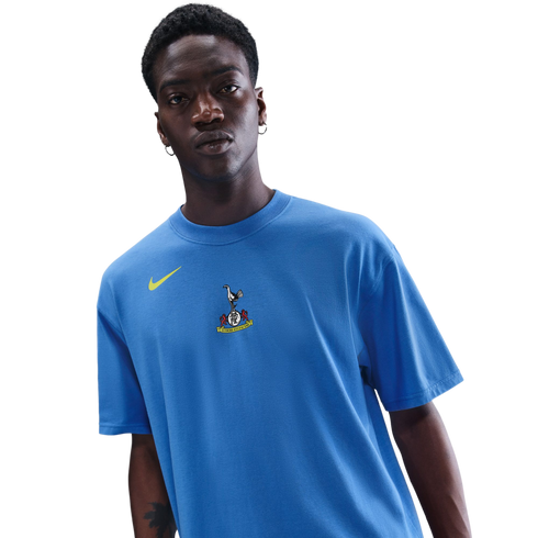 A man wearing a blue Nike t-shirt with a Tottenham Hotspur crest, against a black background.