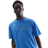 A man wearing a blue Nike t-shirt with a Tottenham Hotspur crest, against a black background.