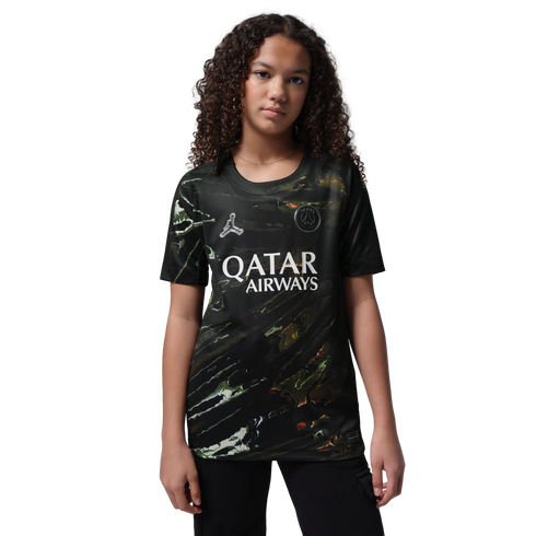A young person with curly hair wearing a black marbled Paris Saint-Germain soccer jersey, standing against a black background.