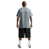 Back view of a man wearing a grey t-shirt with "Chelsea" in white gothic font, black cargo shorts, white socks, and sneakers against a black background.