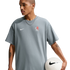A person with arm tattoos wearing a grey Nike Chelsea FC t-shirt holds a soccer ball against a black background.