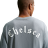 Back view of a person wearing a gray t-shirt with "Chelsea" printed in white Old English lettering across the back, set against a solid black background.