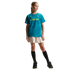A young girl in a teal "LONDON" t-shirt, beige pleated skirt, and black sneakers poses against a black background.