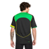 Rear view of a man with curly hair wearing a black soccer jersey with green and yellow accents. He has a tattoo on his left forearm. Plain white background.