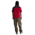 Back view of a person with long dark hair wearing a red, black, and yellow jersey, olive green cargo pants, and white and black sneakers on a white background.