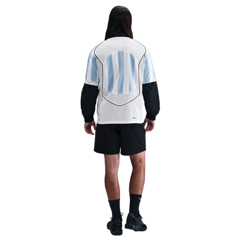 Rear view of a person with long hair in a light blue and white striped soccer jersey, black shorts, and black athletic gear against a white background.