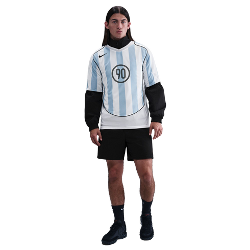 A male model wears a light blue and white striped Nike jersey over a black top, with black shorts and sneakers, posed against a plain white background.