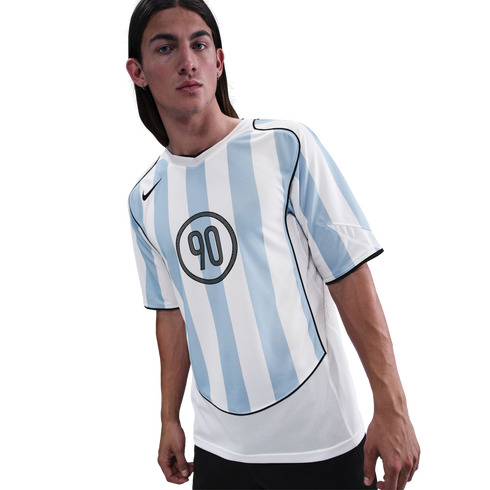 Man with long dark hair posing in a Nike jersey with light blue and white vertical stripes and a circular "90" logo on the chest. Plain white background.