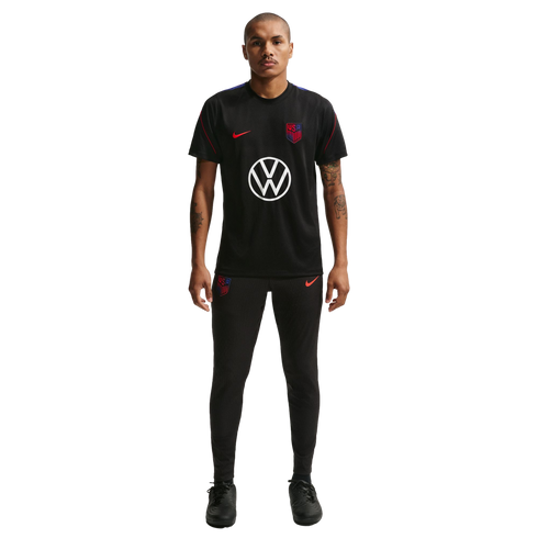 A man stands against a black background wearing a black Nike USA soccer training uniform featuring a large white Volkswagen logo on the shirt.