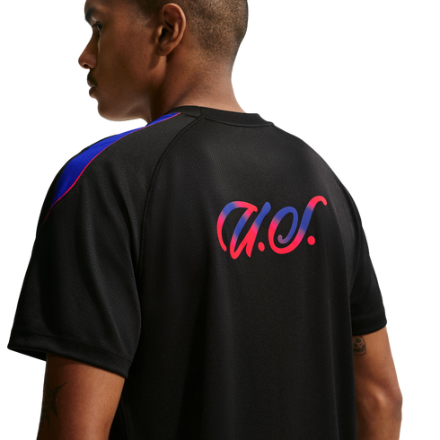 Rear view of a man wearing a black athletic shirt featuring a pink and blue gradient script logo and colorful shoulder stripes.