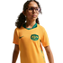 A waist-up portrait of a young girl with curly dark hair and glasses, wearing a yellow and green Australian national soccer team jersey against a black background.