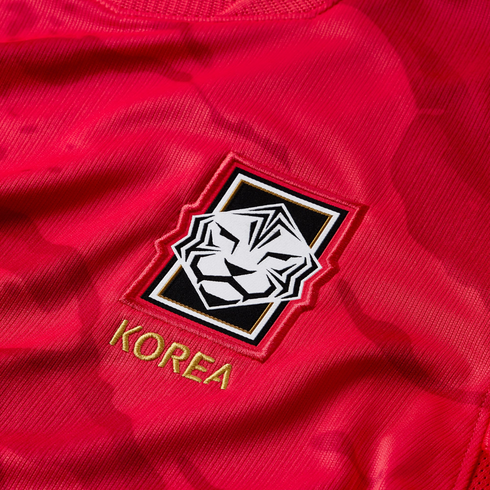 Close-up of a red sports jersey featuring an embroidered patch with a stylized white tiger logo and the word "KOREA" in gold lettering below it.